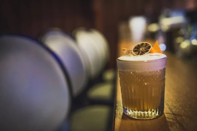 Klasický koktejl s pěnou a sušeným citrusem na baru v Cocktail Roomu